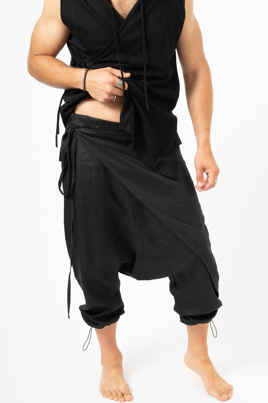 Person wearing a black sleeveless top and baggy black pants on a white background