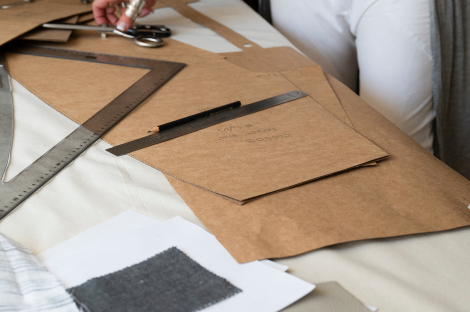 Close-up of a fashion design workspace with pattern papers, a square ruler, scissors, and fabric on a table