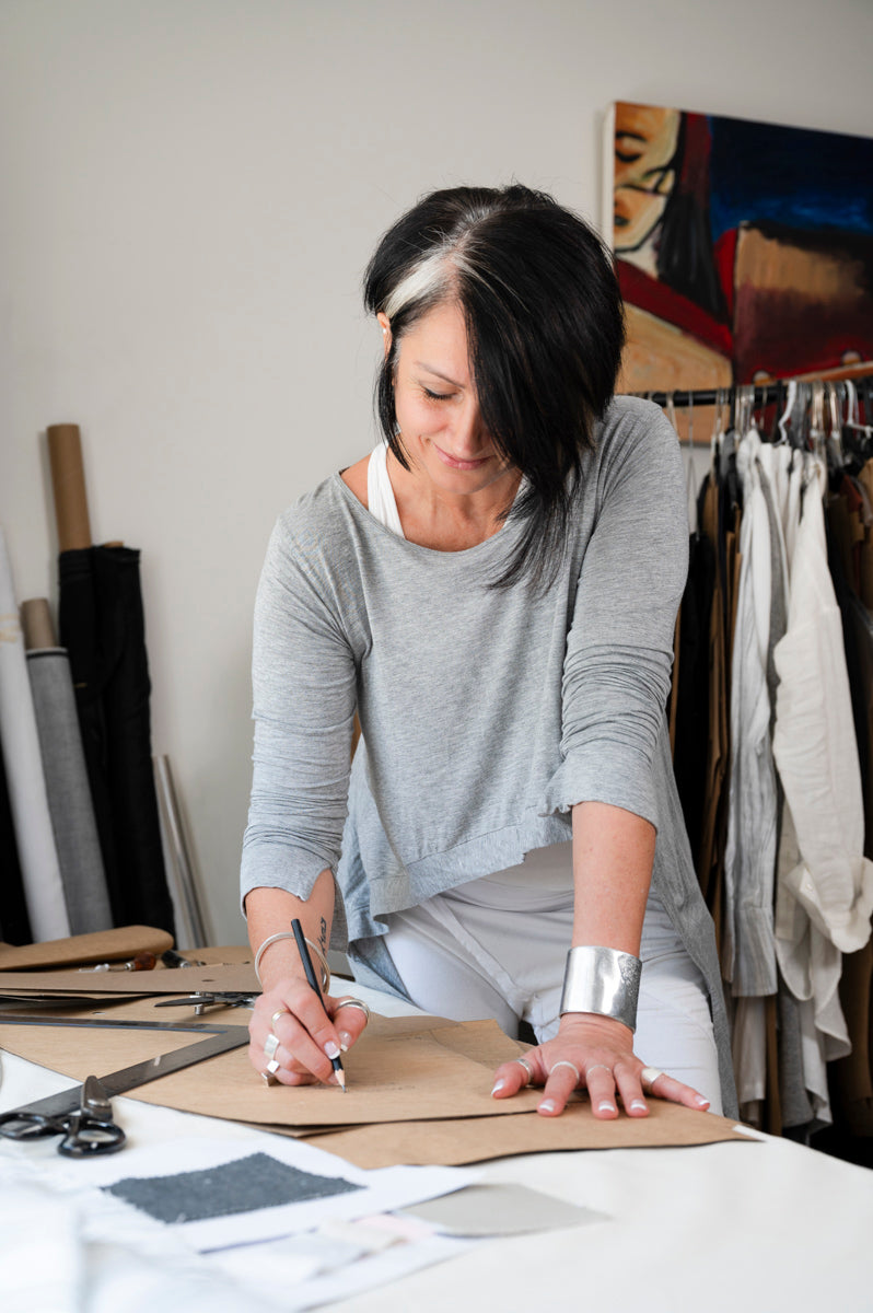 Fashion designer in a grey top working at a studio table, surrounded by fabric samples and design tools