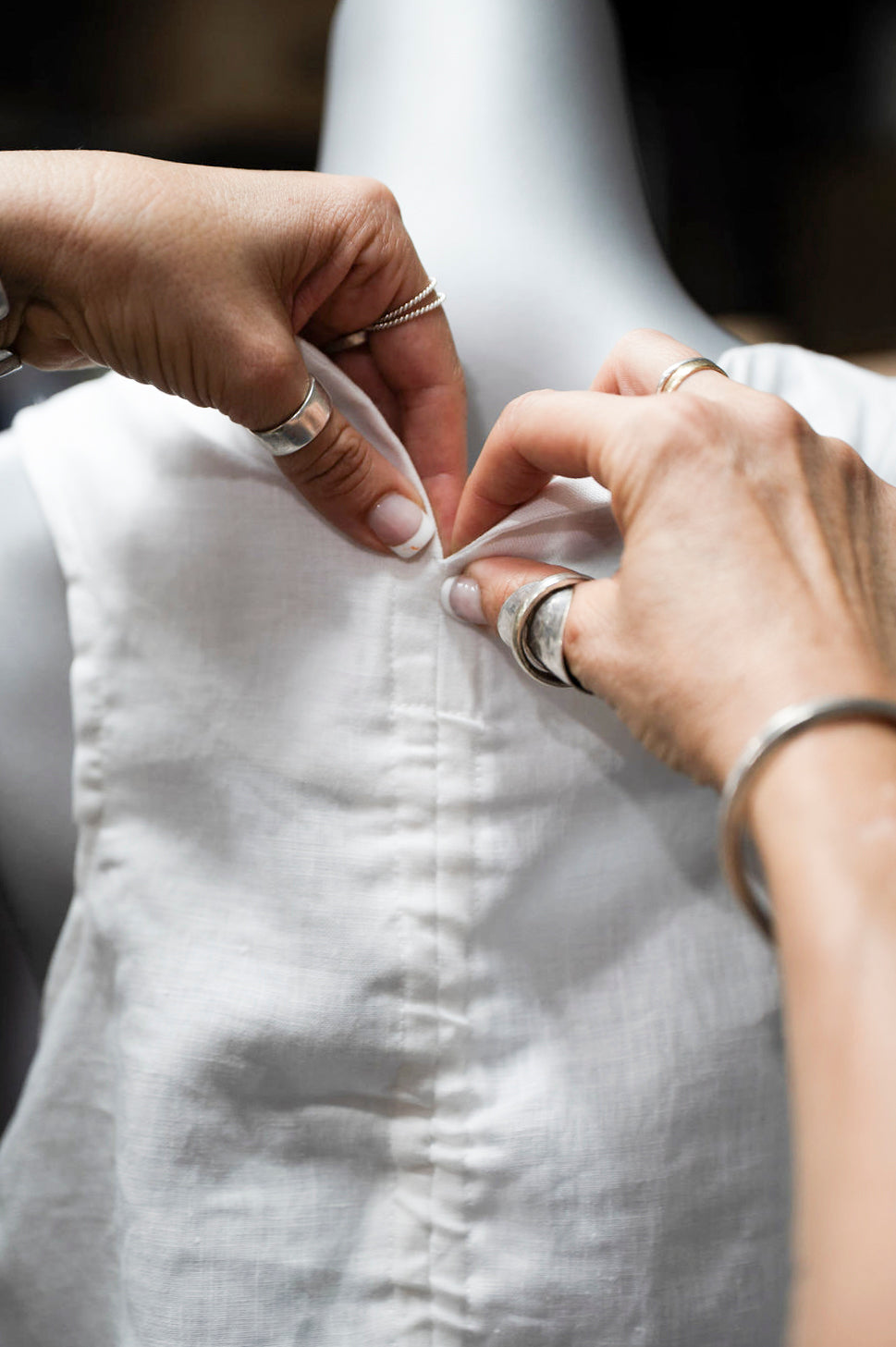 Close-up of hands buttoning up a white linen shirt, showcasing craftsmanship