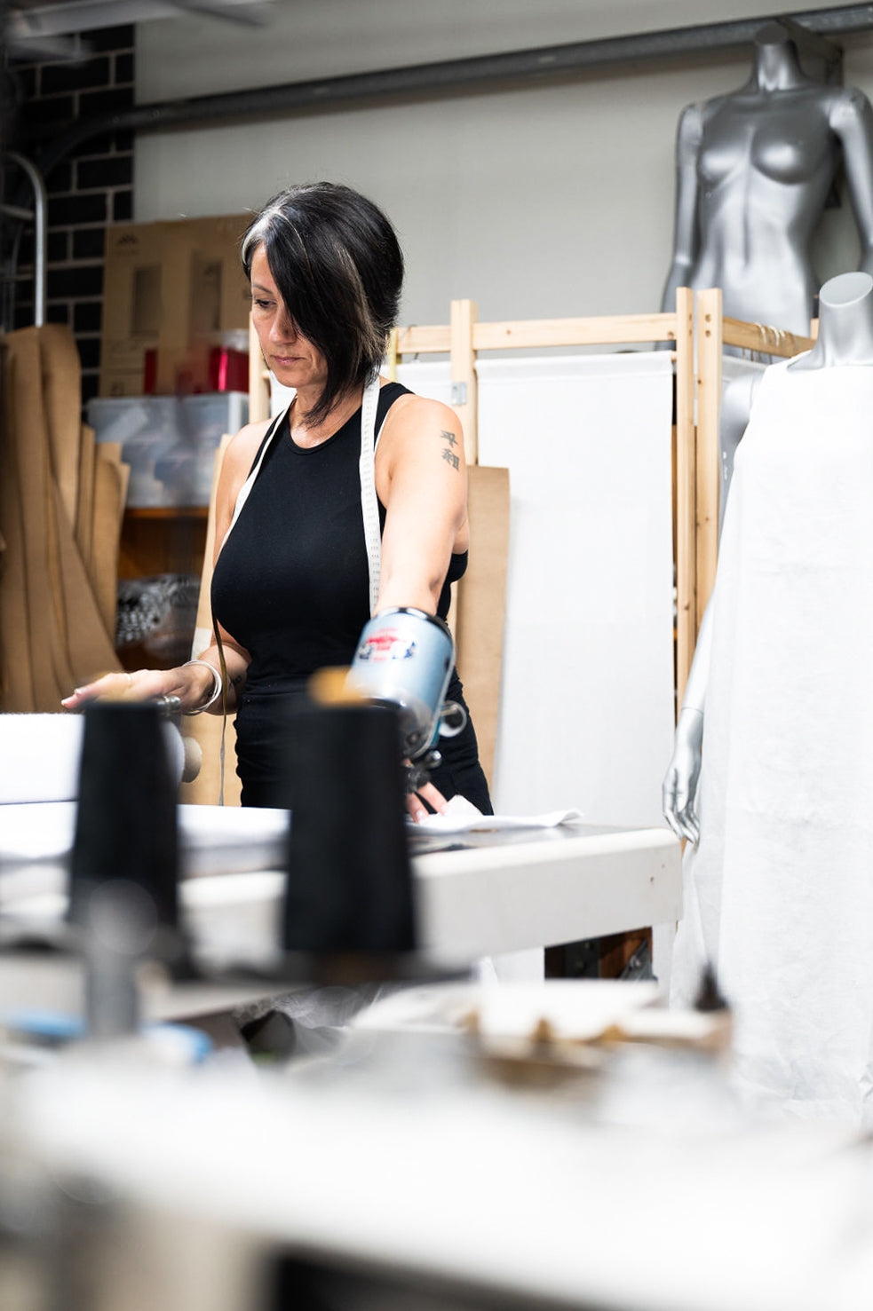 Woman in a black tank top working in a fashion design studio, surrounded by mannequins and sewing equipment