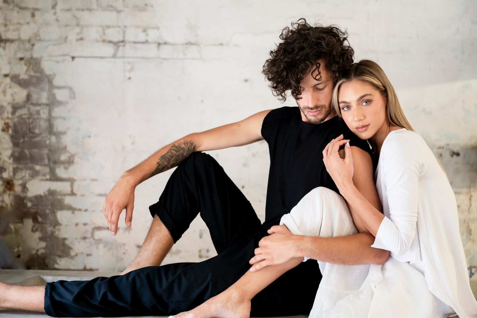 Young couple in a cozy setting, with the man in black attire and the woman in white, sharing a quiet moment