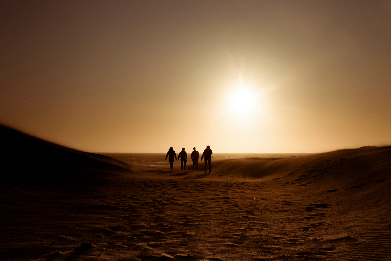 Silhouette of four people walking on desert dunes against a dramatic sunset
